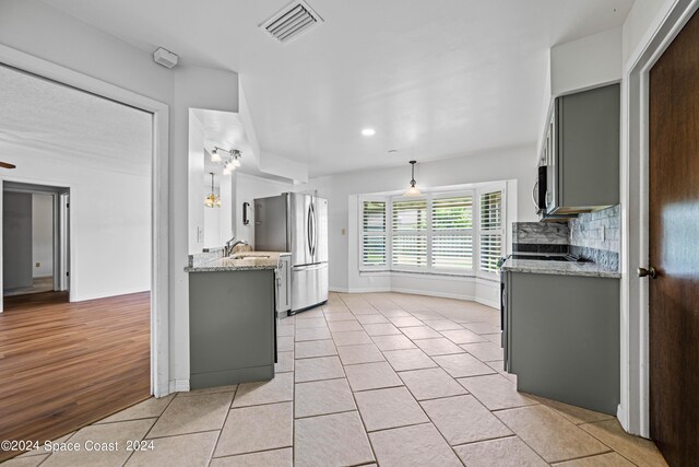 kitchen with stainless steel appliances, light stone countertops, light wood-type flooring, sink, and tasteful backsplash