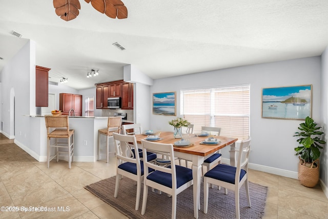 dining space featuring light tile patterned floors, vaulted ceiling, a textured ceiling, and track lighting