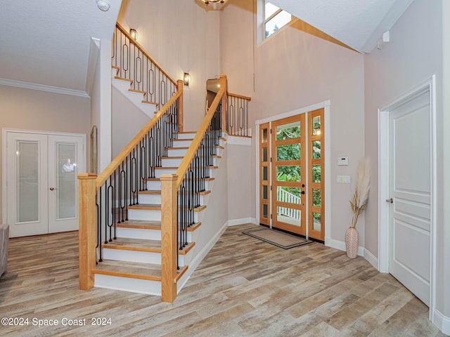 entrance foyer featuring a towering ceiling, french doors, crown molding, and hardwood / wood-style flooring