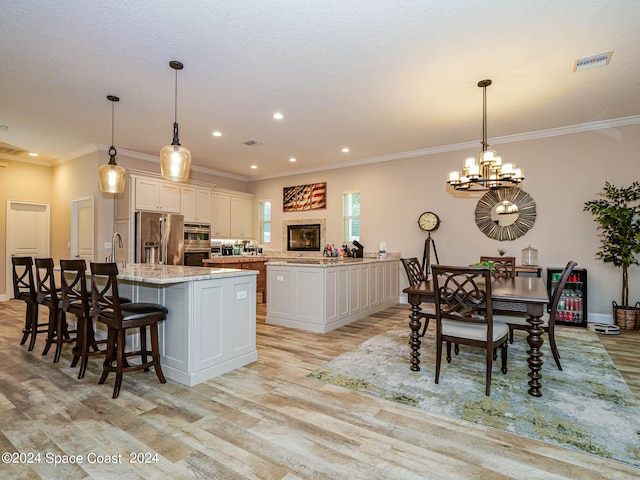 kitchen featuring light stone counters, white cabinetry, appliances with stainless steel finishes, a center island with sink, and light hardwood / wood-style floors