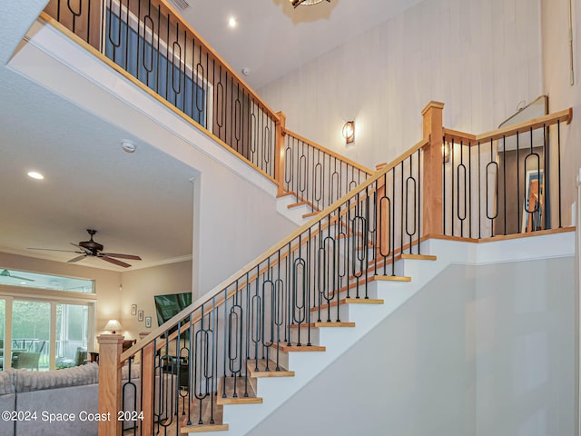 stairs featuring ornamental molding, ceiling fan, and a high ceiling