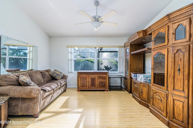 living room with light wood-type flooring, vaulted ceiling, a textured ceiling, and ceiling fan