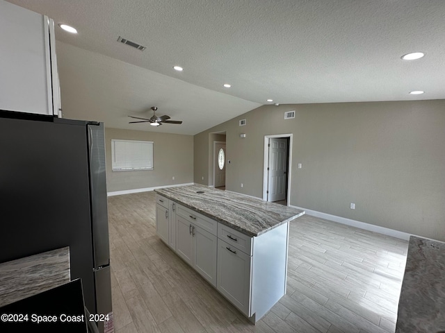 kitchen with ceiling fan, white cabinets, stainless steel refrigerator, vaulted ceiling, and light wood-type flooring