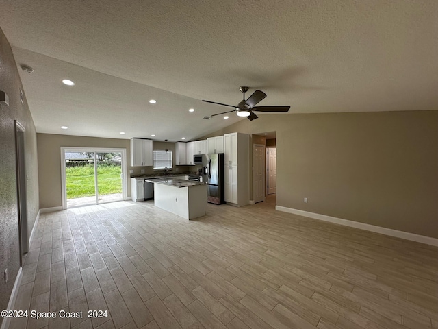 unfurnished living room featuring light wood-type flooring, a textured ceiling, sink, ceiling fan, and vaulted ceiling