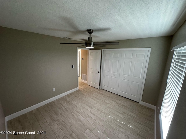 unfurnished bedroom with ceiling fan, light hardwood / wood-style flooring, a textured ceiling, and a closet