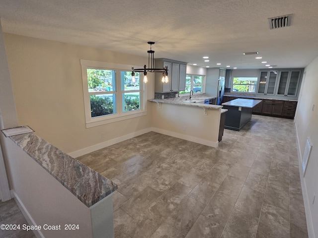 kitchen with decorative light fixtures, a textured ceiling, kitchen peninsula, built in fridge, and light stone countertops