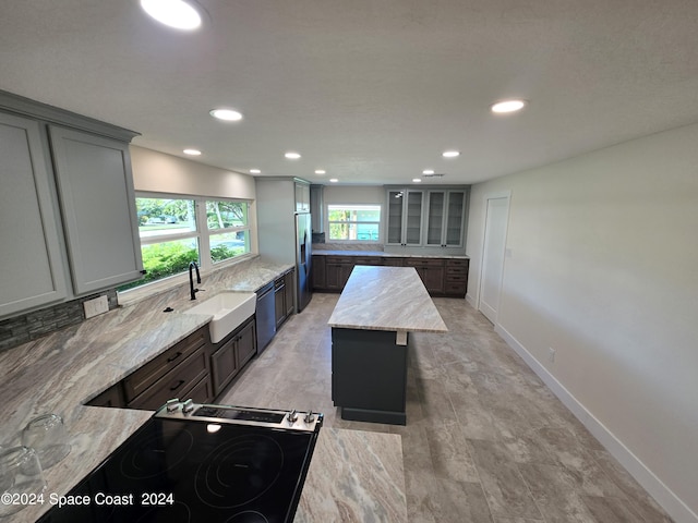 kitchen featuring a kitchen island, appliances with stainless steel finishes, sink, gray cabinetry, and light stone counters