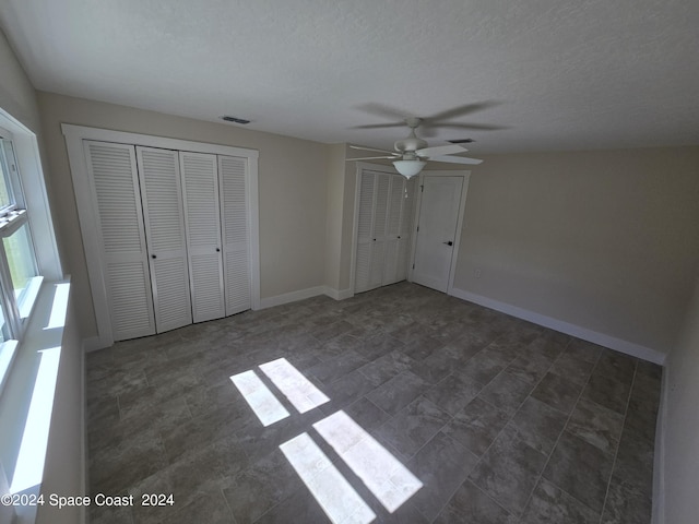 unfurnished bedroom featuring ceiling fan, a textured ceiling, and two closets