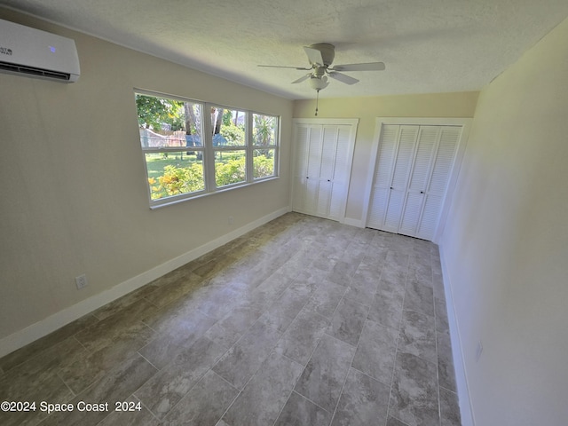 unfurnished bedroom with ceiling fan, a wall mounted AC, a textured ceiling, and two closets