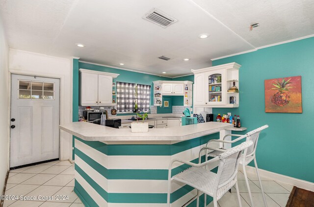 kitchen with white cabinets, light tile patterned floors, crown molding, kitchen peninsula, and a breakfast bar area