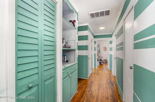 hall with dark wood-type flooring, a textured ceiling, and ornamental molding