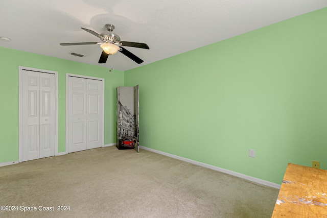 unfurnished bedroom with ceiling fan, two closets, and light colored carpet