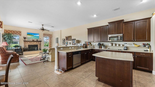 kitchen with a fireplace, light tile patterned floors, stainless steel appliances, ceiling fan, and kitchen peninsula