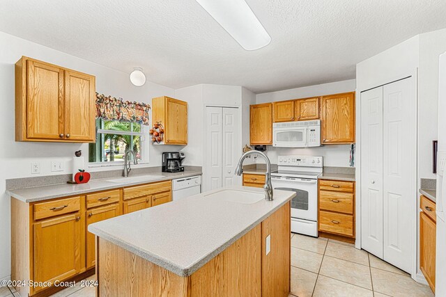 kitchen with sink, white appliances, an island with sink, and light tile patterned floors