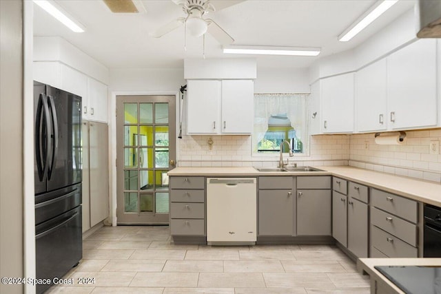 kitchen with white dishwasher, gray cabinetry, a sink, white cabinets, and light countertops