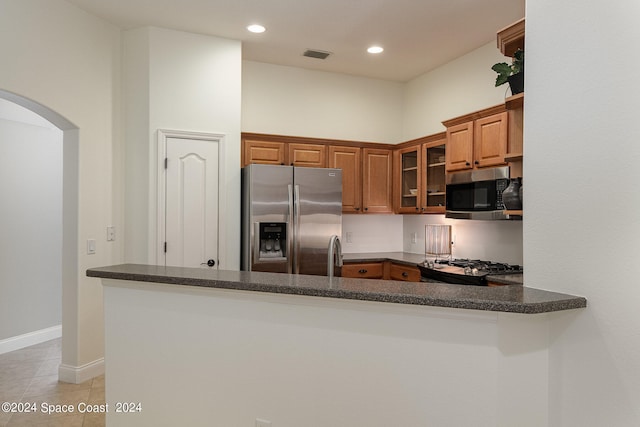 kitchen with appliances with stainless steel finishes, light tile patterned flooring, dark stone counters, and kitchen peninsula