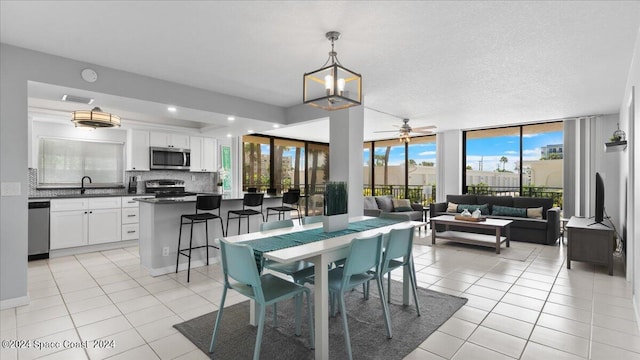 tiled dining area featuring sink, a wall of windows, ceiling fan with notable chandelier, and a wealth of natural light