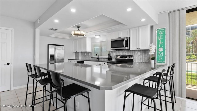 kitchen featuring decorative backsplash, kitchen peninsula, stainless steel appliances, and a raised ceiling