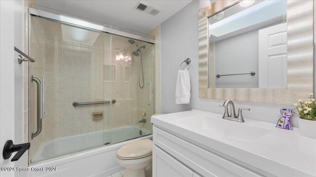 bathroom featuring toilet, bath / shower combo with glass door, vanity, and visible vents