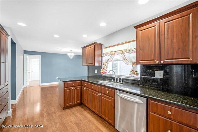 kitchen featuring light hardwood / wood-style flooring, stainless steel dishwasher, sink, kitchen peninsula, and dark stone countertops