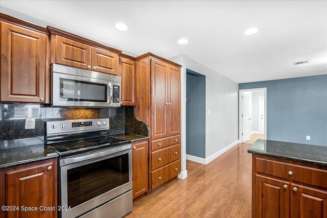 kitchen featuring appliances with stainless steel finishes, dark stone counters, light wood-type flooring, and tasteful backsplash