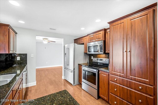 kitchen with dark stone counters, backsplash, light hardwood / wood-style flooring, ceiling fan, and stainless steel appliances