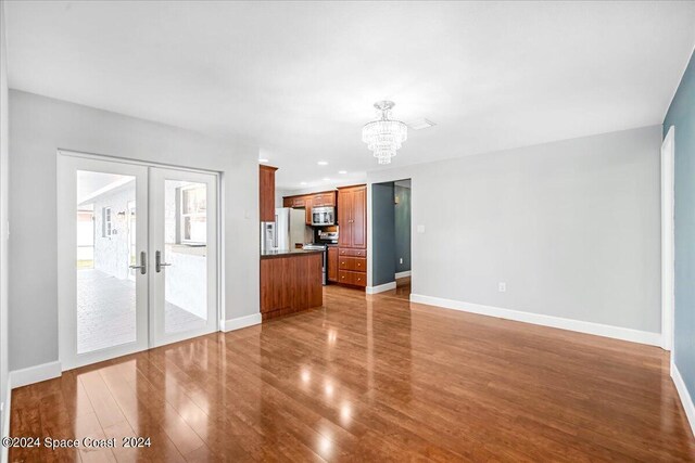 unfurnished living room featuring an inviting chandelier, wood-type flooring, and french doors