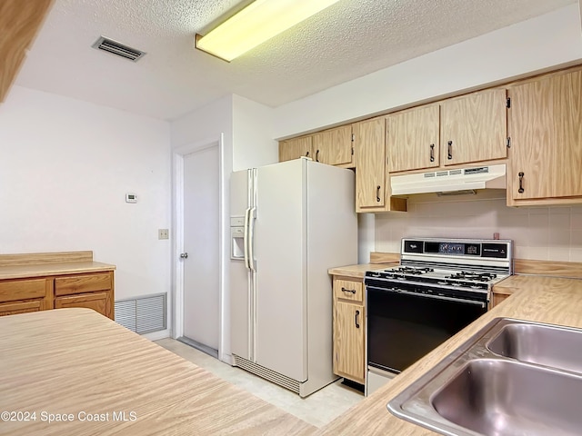 kitchen with white appliances, light brown cabinetry, sink, and a textured ceiling