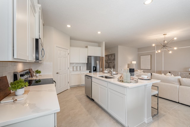 kitchen with appliances with stainless steel finishes, a kitchen island with sink, sink, white cabinetry, and light tile patterned flooring