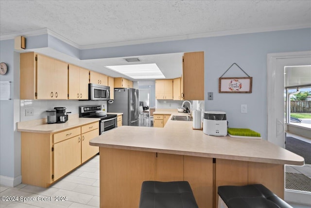 kitchen with light brown cabinets, a peninsula, stainless steel appliances, a sink, and light countertops