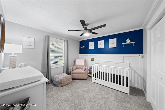 carpeted bedroom featuring ornamental molding, a nursery area, a wainscoted wall, and a textured ceiling