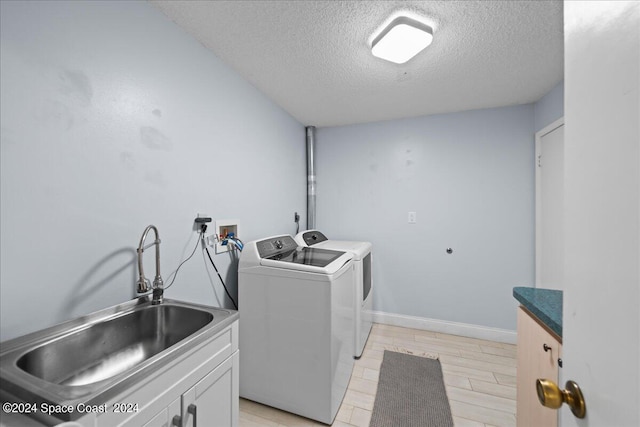 clothes washing area with cabinet space, baseboards, independent washer and dryer, a textured ceiling, and a sink