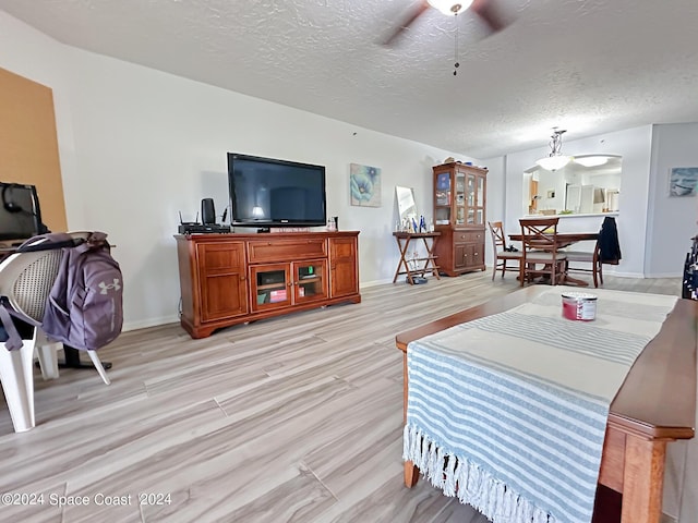 living room with ceiling fan, light wood-type flooring, and a textured ceiling