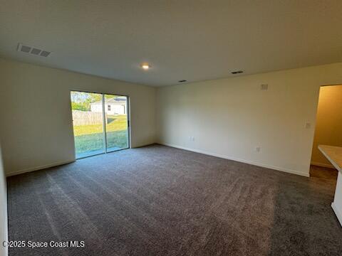 spare room featuring baseboards, visible vents, and dark colored carpet