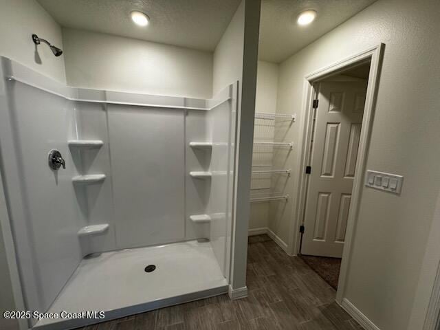 bathroom featuring a textured ceiling, a shower, wood finished floors, and baseboards