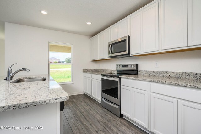 kitchen with stainless steel appliances, sink, white cabinets, light stone counters, and dark hardwood / wood-style flooring