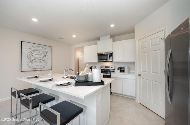 kitchen with appliances with stainless steel finishes, a breakfast bar, an island with sink, white cabinets, and light tile patterned floors