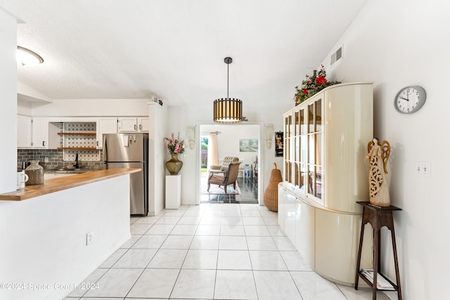 kitchen featuring white cabinetry, stainless steel refrigerator, tasteful backsplash, pendant lighting, and light tile patterned floors