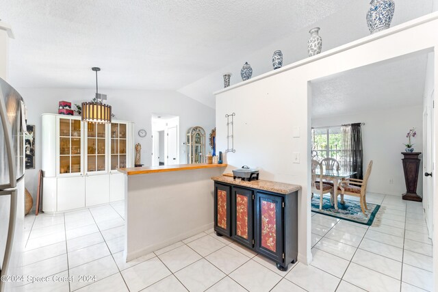 kitchen with kitchen peninsula, lofted ceiling, a textured ceiling, and light tile patterned floors