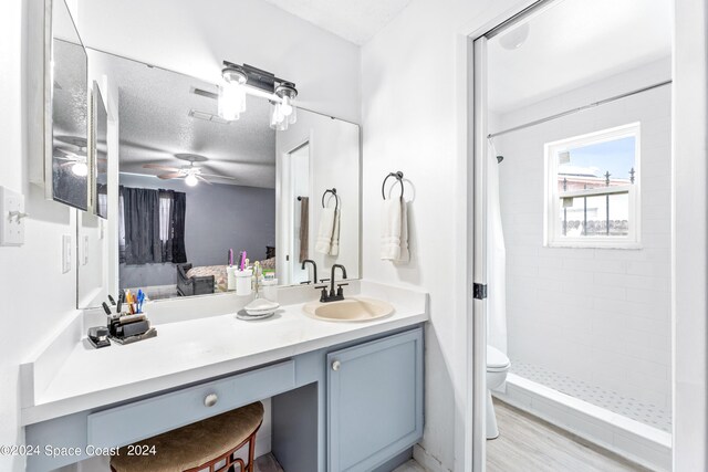 bathroom featuring ceiling fan, toilet, vanity, curtained shower, and a textured ceiling