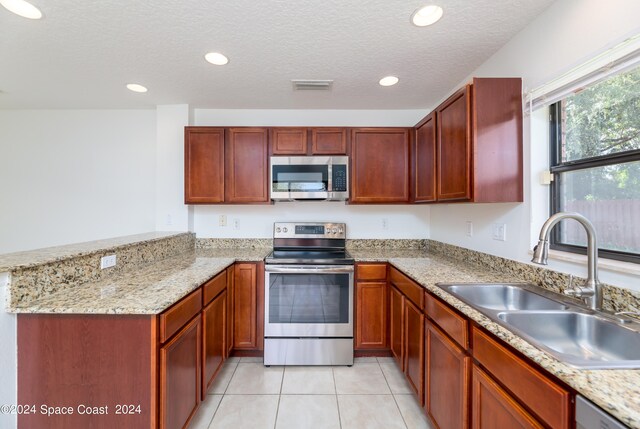 kitchen with light tile patterned floors, appliances with stainless steel finishes, sink, kitchen peninsula, and light stone counters