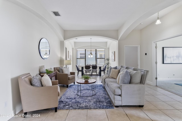 living room with arched walkways, light tile patterned flooring, visible vents, baseboards, and an inviting chandelier