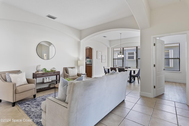 living area with light tile patterned floors, baseboards, visible vents, and arched walkways