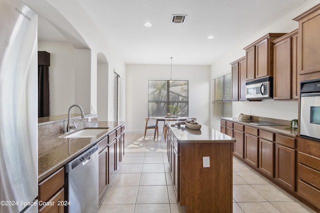 kitchen with light tile patterned floors, stainless steel appliances, a kitchen island, a sink, and visible vents