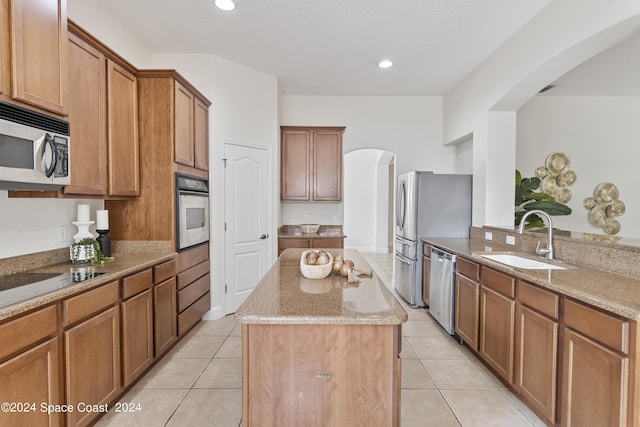 kitchen featuring light stone counters, arched walkways, a center island, appliances with stainless steel finishes, and a sink