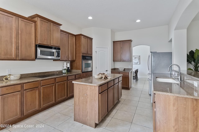 kitchen with light stone counters, light tile patterned flooring, a kitchen island, a sink, and appliances with stainless steel finishes