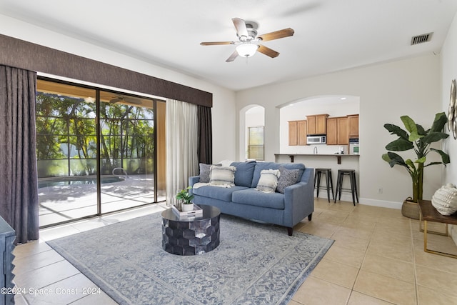 living area featuring light tile patterned floors, visible vents, arched walkways, baseboards, and ceiling fan