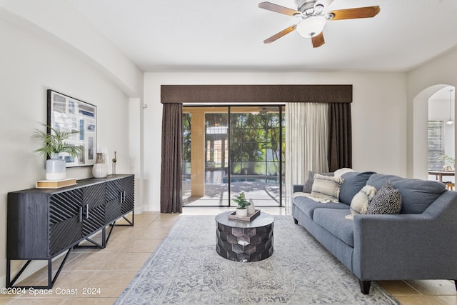 tiled living room with a ceiling fan, arched walkways, and baseboards