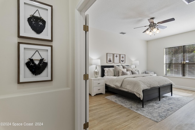 bedroom featuring a textured ceiling, ceiling fan, visible vents, and light wood-style floors