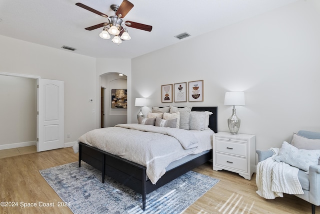 bedroom featuring light wood finished floors, ceiling fan, visible vents, and arched walkways